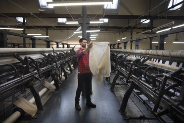 Porträt eines männlichen Webers, der das Gewebe einer alten Webmaschine in einer Textilfabrik untersucht - ISF14085