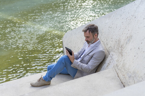 Geschäftsmann sitzt auf Stufen im Freien und benutzt ein Tablet, lizenzfreies Stockfoto