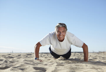 Senior man doing push ups on beach - CUF33203