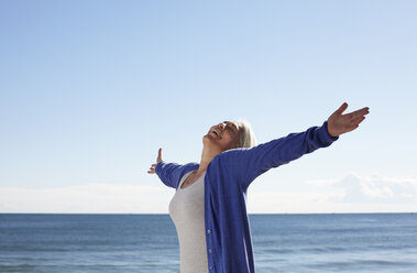 Mature woman on beach with arms outspread - CUF33221