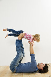 Studio shot of father lifting up daughter whilst lying on back - CUF33286