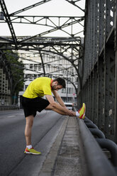 Junger männlicher Läufer, der sich auf einer Brücke die Beine vertritt - CUF33367