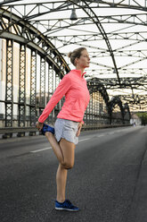 Junge Läuferin beim Dehnen auf einer Brücke - CUF33377