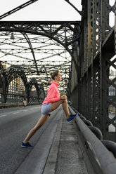 Junge Läuferin streckt die Beine auf einer Brücke - CUF33380