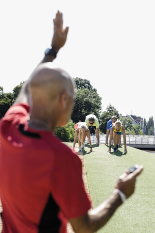 Älterer Mann bereitet eine Gruppe erwachsener Läufer an der Startlinie vor, lizenzfreies Stockfoto