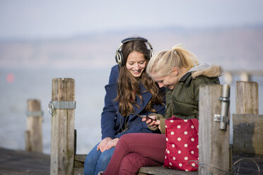 Teenager-Mädchen sitzen auf dem Steg und hören Musik - CUF33387