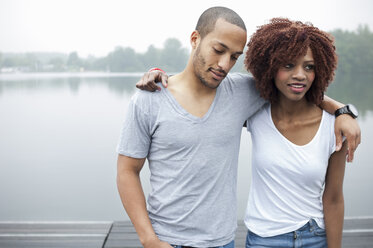 Portrait of young couple by lake with arms around each other - CUF33404