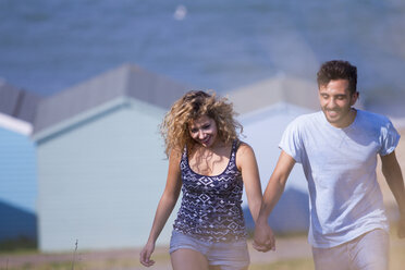 Junges Paar hält Hände mit Strandhütten im Hintergrund - CUF33423