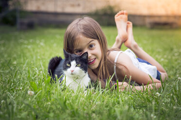 Porträt eines kleinen Mädchens mit Katze auf einer Wiese liegend - LVF07124