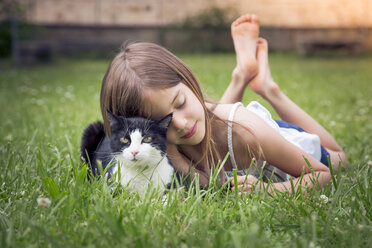 Kleines Mädchen kuschelt mit Katze auf einer Wiese - LVF07125
