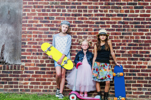 Porträt von drei Mädchen mit Skateboards und Motorroller vor einer Backsteinmauer - ISF14133