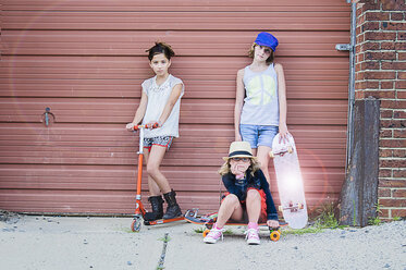 Porträt von drei Mädchen mit Skateboards und Rollern vor einer Garage - ISF14134
