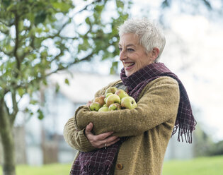Glückliche ältere Frau mit einem Arm voller Äpfel - CUF33564