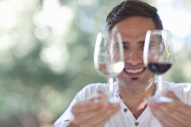 Young male waiter holding up glasses of red and white wines - CUF33606