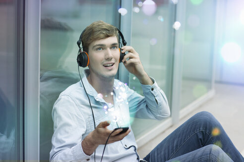 Junger Mann mit Kopfhörern und Smartphone mit Lichtern, die aus ihm herauskommen - CUF33611