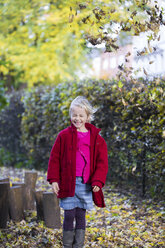 Portrait of grinning little girl throwing leaves in the air in autumn - JFEF00881