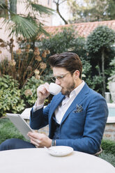 Elegant businessman drinking coffee and using tablet in a garden cafe - ALBF00538