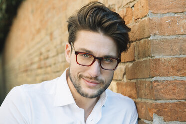 Portrait of a smiling man wearing glasses at brick wall - ALBF00573