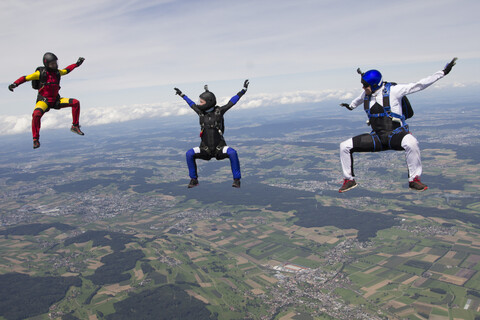 Team von drei Fallschirmspringern in Sitzflugposition über Buttwil, Luzern, Schweiz, lizenzfreies Stockfoto