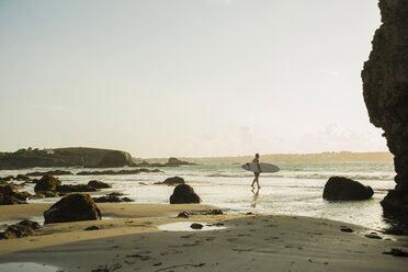 Mature man walking towards sea, holding surf board - CUF33697