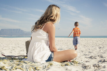 Mittlere erwachsene Mutter beobachtet ihren kleinen Sohn beim Spielen am Strand, Kapstadt, Westkap, Südafrika - CUF33708