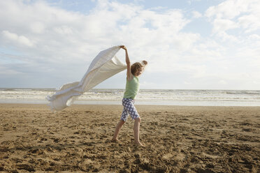 Mädchen hält Decke am windigen Strand hoch, Camber Sands, Kent, UK - CUF33718