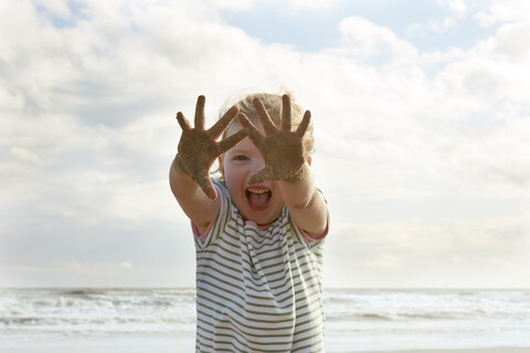 Mädchen hält sandige Hände am Strand hoch, Camber Sands, Kent, UK, lizenzfreies Stockfoto