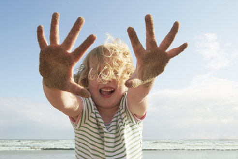 Mädchen hält sandige Hände am windigen Strand hoch, Camber Sands, Kent, UK - CUF33721