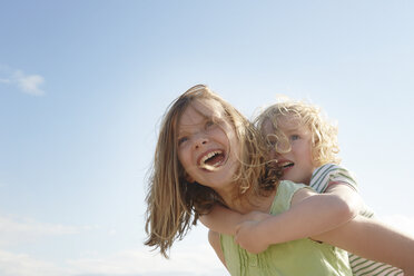 Low angle view of girl giving sister piggy back at coast - CUF33724