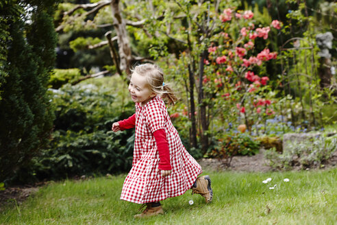 Junges Mädchen in kariertem Kleid läuft im Garten - CUF33741