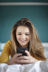 Teenage girl in bedroom texting on smartphone - CUF33777