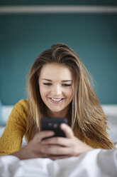 Teenager-Mädchen im Schlafzimmer, das eine SMS auf dem Smartphone schreibt - CUF33777