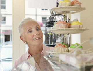 Ältere Frau betrachtet Cupcakes in einem Cafe - CUF33813