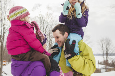 Mother and father carrying daughters in snow - CUF33920