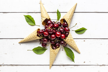 Arrangement of five ice cream cones and pile of cherries on white wood - SARF03795