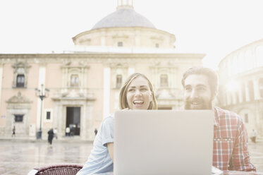 Young couple looking at laptop in sidewalk cafe, Plaza de la Virgen, Valencia, Spain - CUF34014