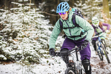 Zwei Mountainbikerinnen fahren im Schnee durch den Wald - CUF34023