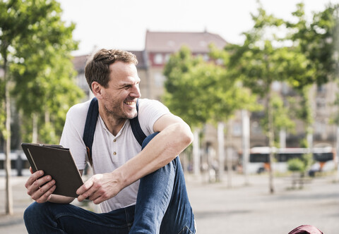 Lächelnder Mann sitzt im Freien mit Tablet, lizenzfreies Stockfoto