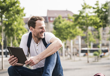 Smiling man sitting outdoors with tablet - UUF14282