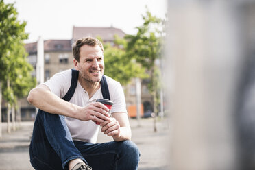 Porträt eines lächelnden Mannes mit Kaffee zum Mitnehmen in der Stadt - UUF14283