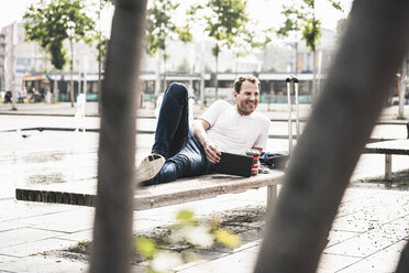 Smiling man lying on bench with tablet - UUF14287