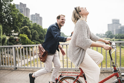 Glückliches Paar beim Überqueren einer Brücke mit dem Fahrrad und zu Fuß - UUF14302