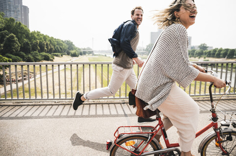 Glückliches Paar beim Überqueren einer Brücke mit dem Fahrrad und zu Fuß, lizenzfreies Stockfoto