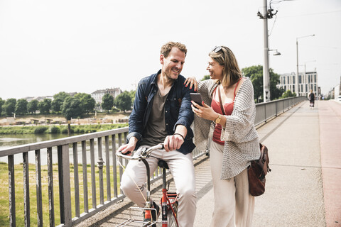 Glückliches Paar mit Fahrrad und Mobiltelefon beim Überqueren einer Brücke, lizenzfreies Stockfoto