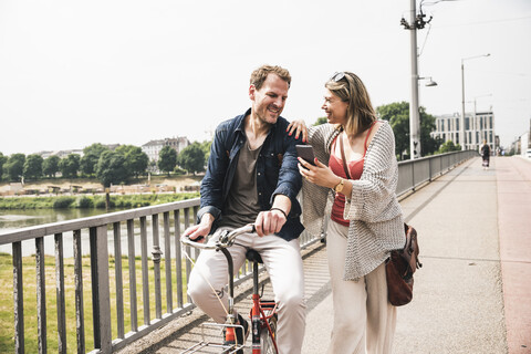 Happy couple with bicycle and cell phone crossing a bridge stock photo