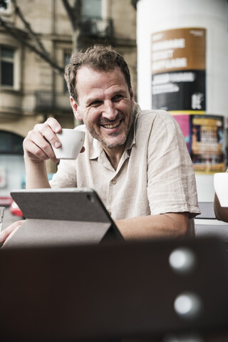 Lächelnder Mann mit Tablet und Kaffee in einem Straßencafé, lizenzfreies Stockfoto