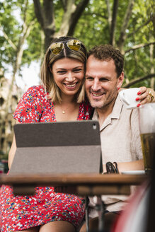Lächelndes Paar teilt sich ein Tablet in einem Café im Freien - UUF14314