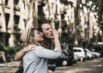 Couple blowing soap bubbles in the city together - UUF14321