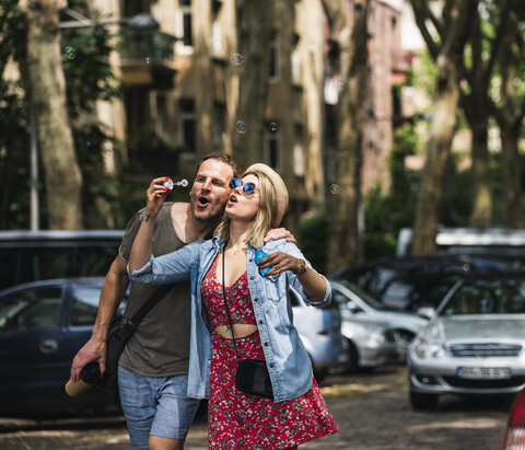 Paar, das gemeinsam Seifenblasen in der Stadt bläst, lizenzfreies Stockfoto
