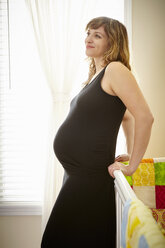 Schwangere Frau lehnt an Krippe im Kinderzimmer - ISF14235